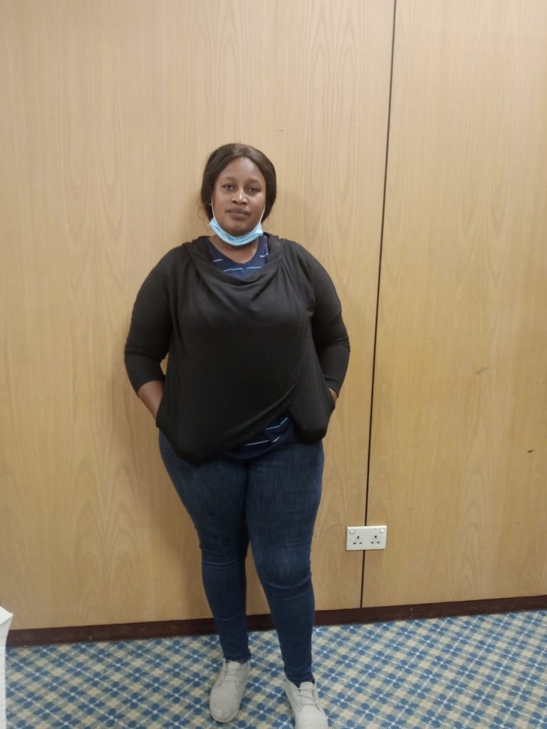 A lady posing infront of a brown wall in a room