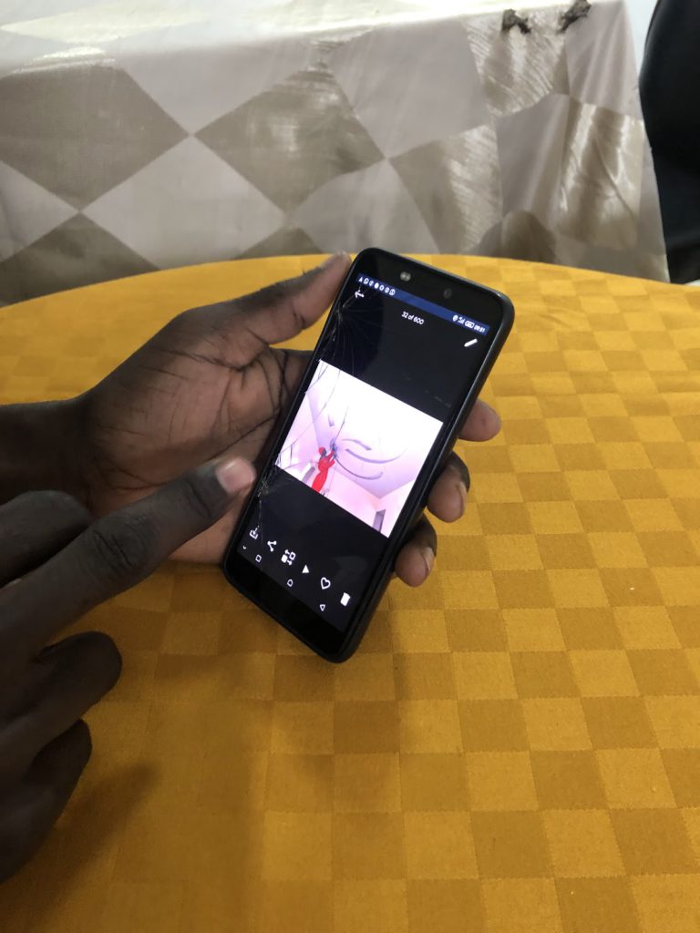 A close-up of a hand holding a phone showing pictures of men working. The background is a table with an orange checked tablecloth.